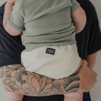 Tattooed arm holding baby wearing a reusable nappy